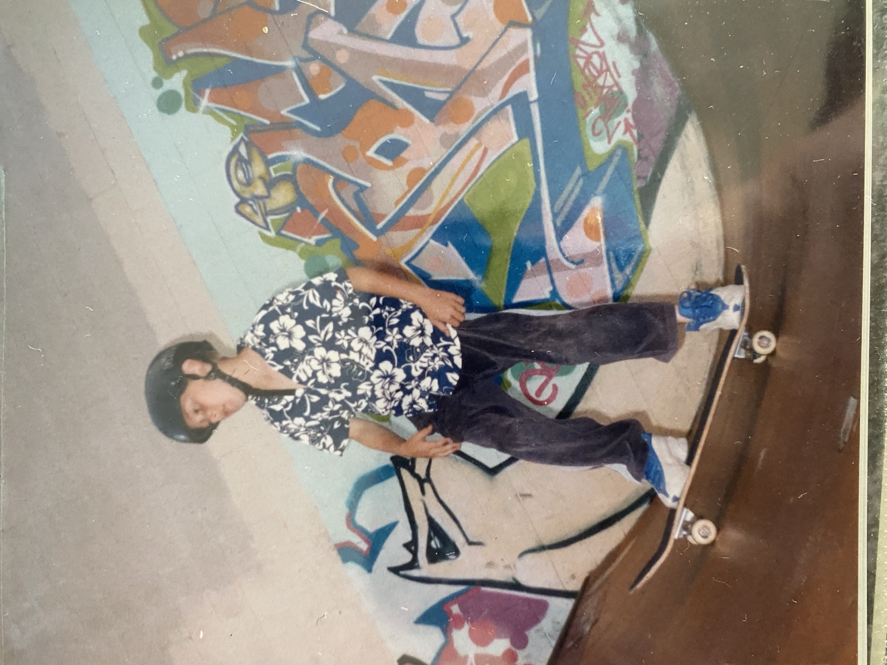 A young Haden standing on a skate ramp in front of colorful skatepark graffiti.