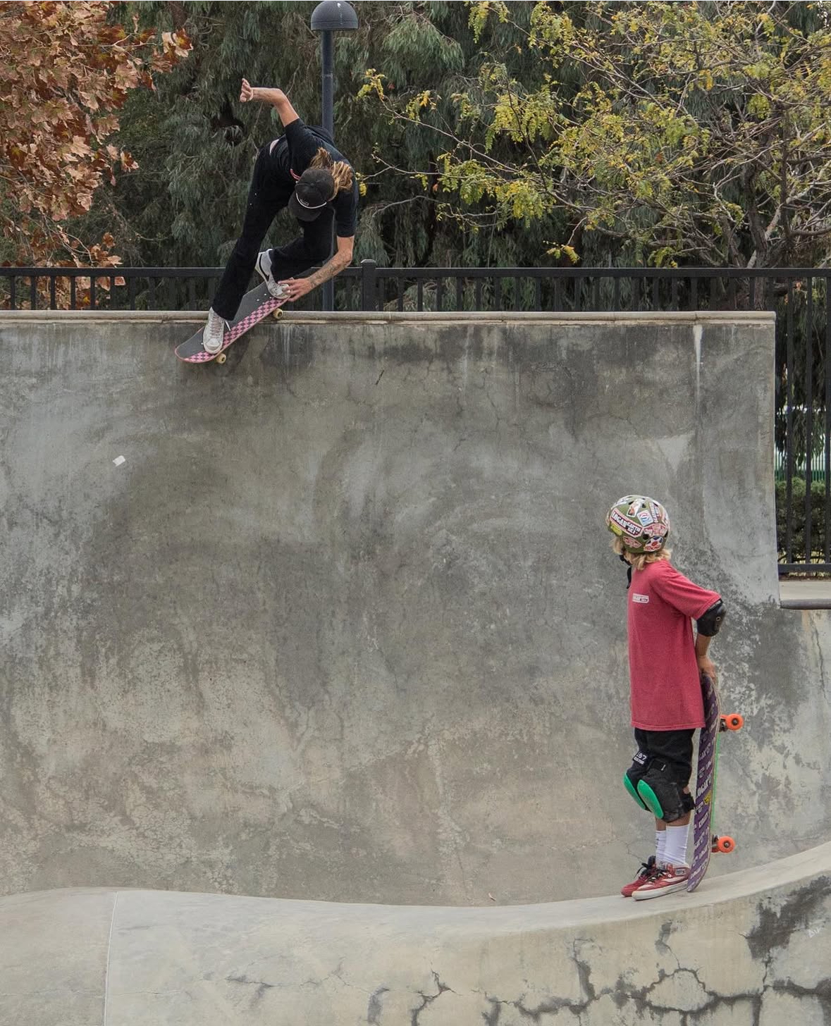 A young skater watches Haden demonstrate a beginner-friendly move in a skate bowl.